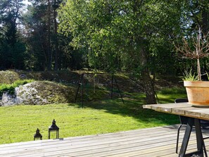 A wooden deck with a table and chairs, surrounded by a grassy area with trees and a swing set.