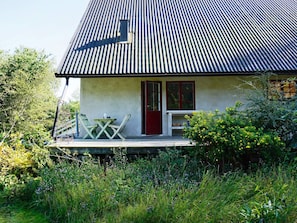 A house with a corrugated metal roof, a front porch with a table and chairs, and a red door. - 7 Person Holiday Home in Djurhamn (Djurhamn)