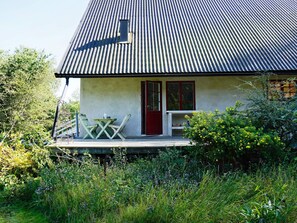 A house with a corrugated metal roof, a front porch with a table and chairs, and a red door.