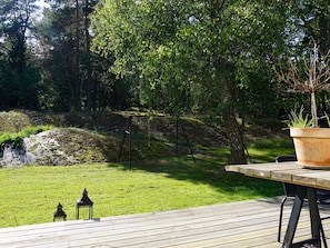 A wooden deck with a table and chairs, surrounded by a grassy area with trees and a swing set. - 7 Person Holiday Home in Djurhamn (Djurhamn)