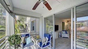 A balcony with a ceiling fan, a seating area with a table, and a view of the interior.