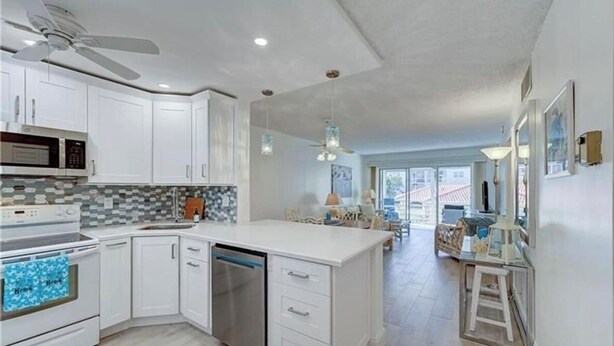 A modern kitchen with white cabinets, a microwave, stove, and dishwasher. There is a dining area with a table and chairs visible in the background.