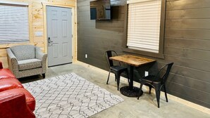 A room with a wooden ceiling, a grey door, a TV mounted on the wall, a small table with chairs, and a red sofa. - Knotty Squirrel Unit 9 Standard King Suite (Mountain View)