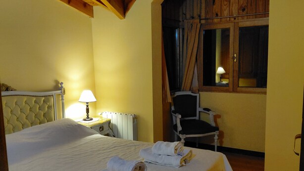 A bedroom with a large bed, a chair, a lamp, and a window with curtains.