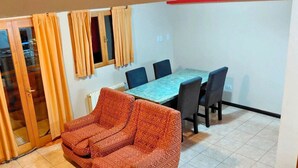 A dining area with a table and chairs, a sofa, and a sliding glass door with curtains.
