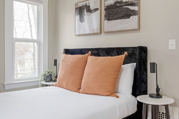 A bedroom with a bed, two pillows, a bedside table, a lamp, and two framed pictures on the wall. - City Charmer With A Modern Twist (Grand Rapids)
