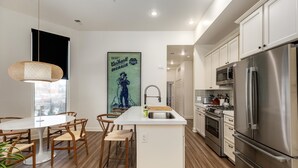 Une cuisine moderne dotée d’un îlot central, d’appareils électroménagers en acier inoxydable, de planchers en bois et d’un coin repas avec des chaises et une table.