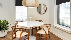 Un coin repas comprenant une table ronde, quatre chaises en bois, un luminaire suspendu, un miroir rond et une plante en pot.
