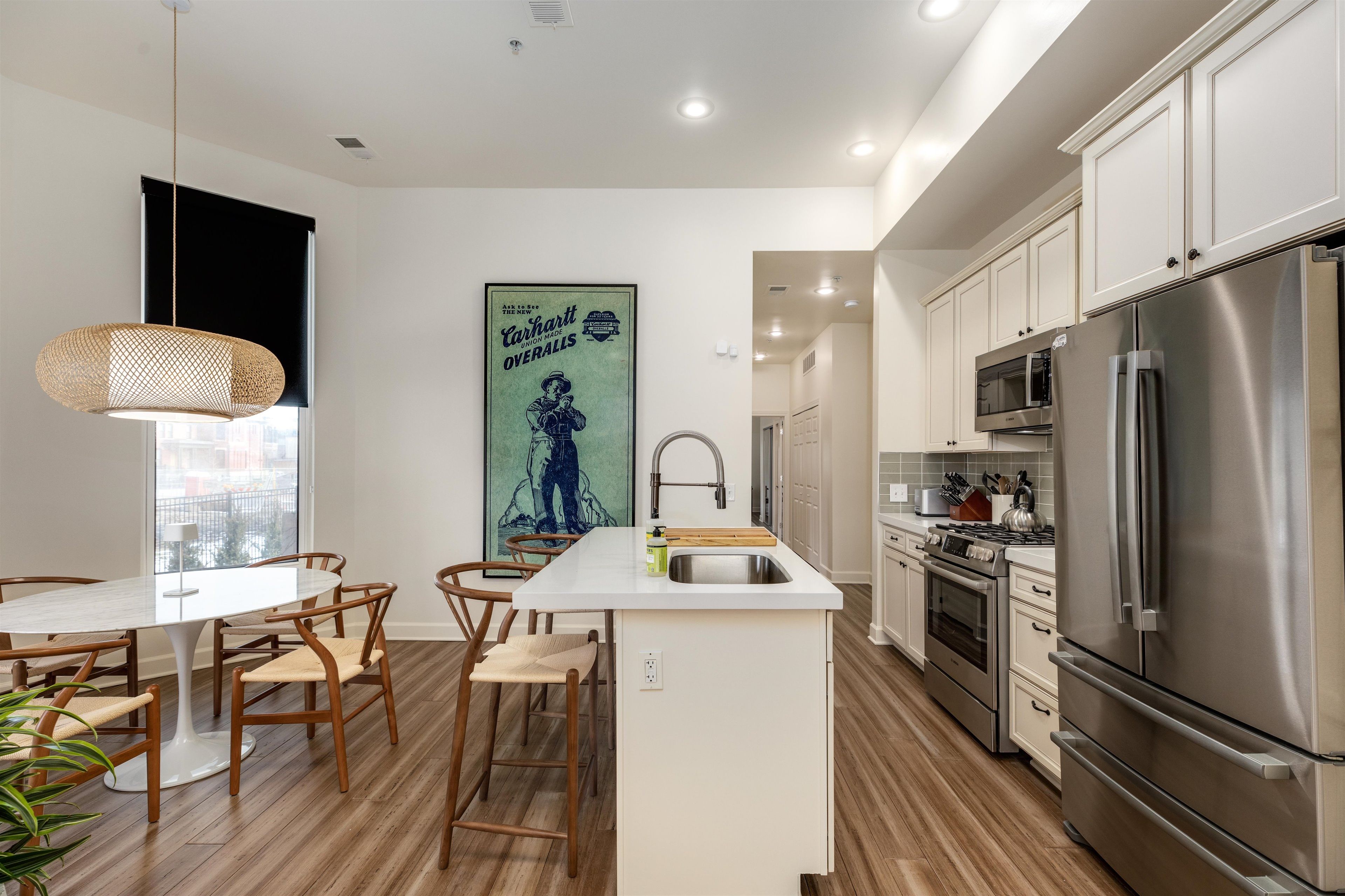 Una cocina moderna con una isla central, electrodomésticos de acero inoxidable, suelo de madera y un comedor con sillas y una mesa.