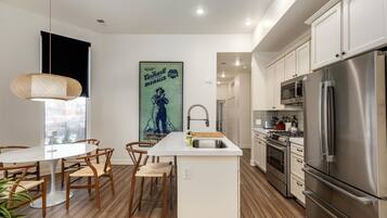 Una cocina moderna con una isla central, electrodomésticos de acero inoxidable, suelo de madera y un comedor con sillas y una mesa.