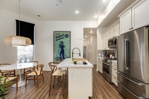 Een moderne keuken met een centraal eiland, roestvrijstalen apparatuur, houten vloeren en een eetgedeelte met stoelen en een tafel.