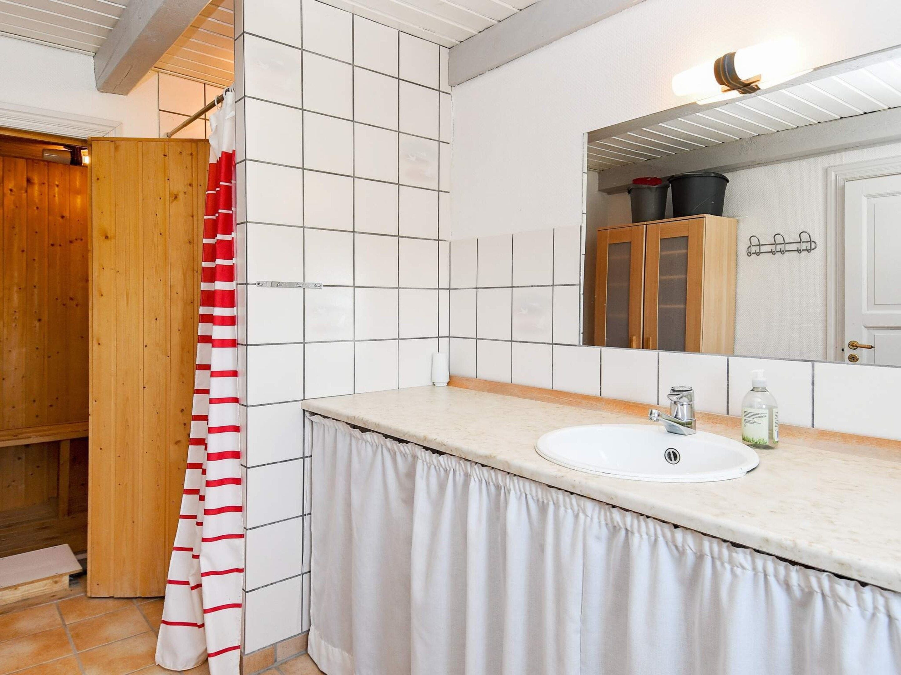 Un baño con lavamanos blanco, armarios de madera y cortina de ducha.