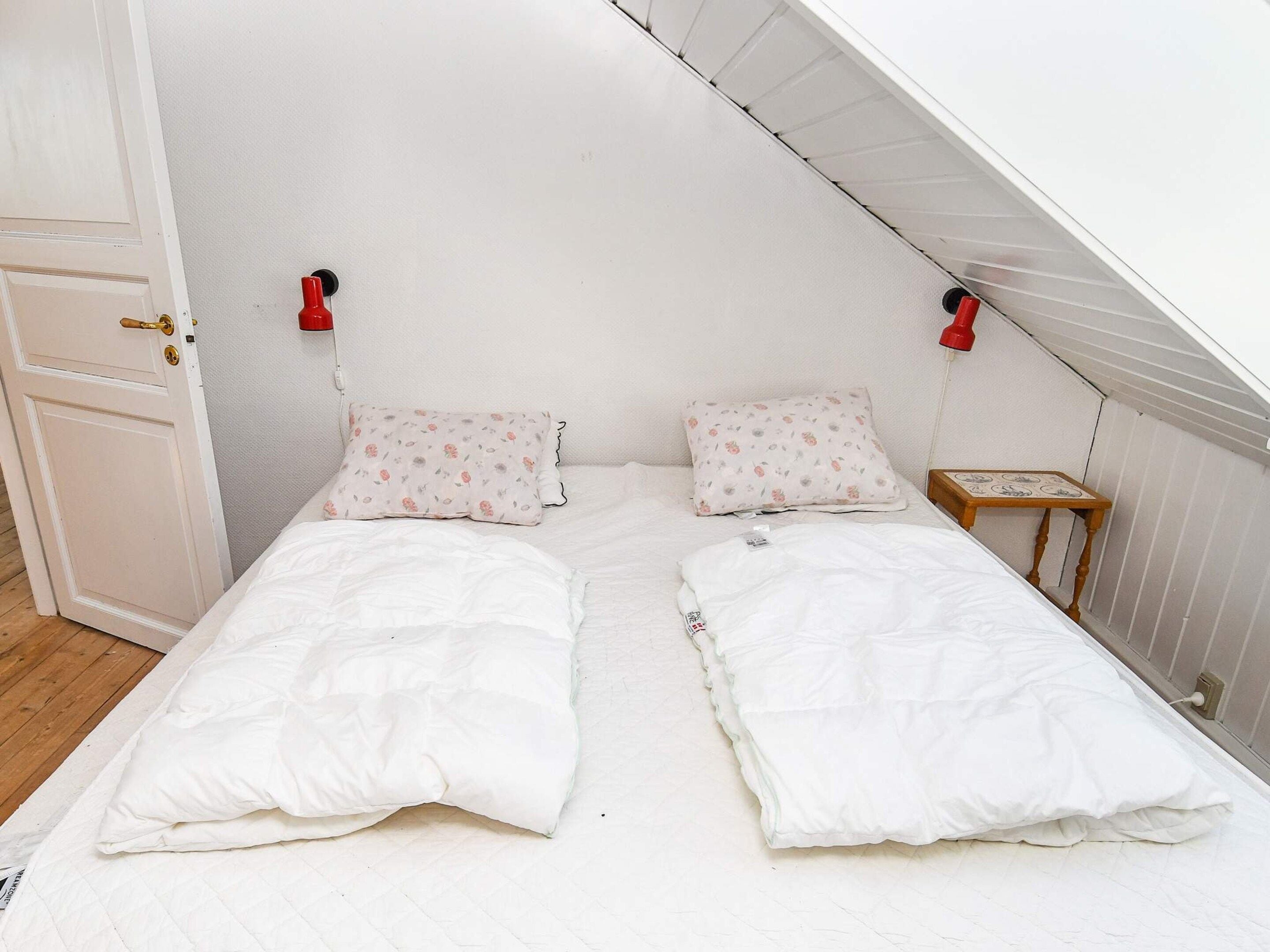 A small, white, two-bed room with a sloped ceiling, two bedside tables, and floral-patterned pillows.