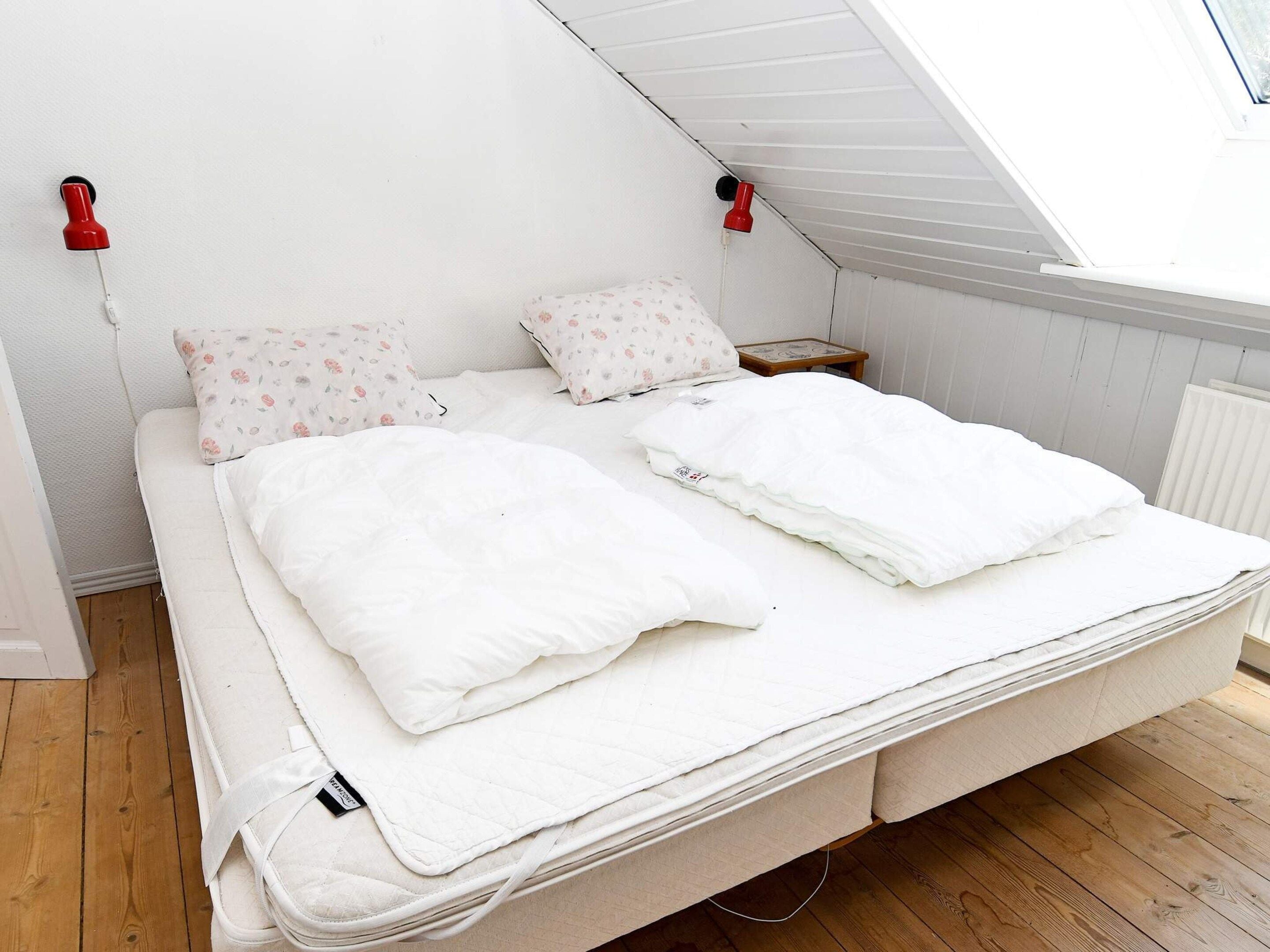 A bed with white bedding and floral-patterned pillows, a wooden floor, and a skylight above.