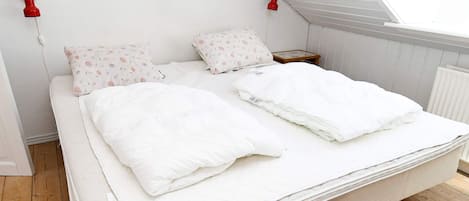 A bed with white bedding and floral-patterned pillows, a wooden floor, and a skylight above.
