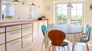 A dining area with a round table, chairs, and a kitchen area with cabinets and a counter.