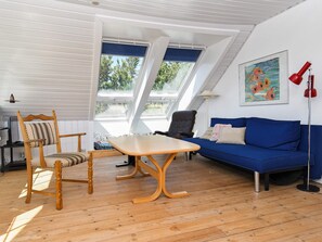 A modern living room with a wooden floor, a blue sofa, a wooden chair, a table, and a ceiling with skylights.