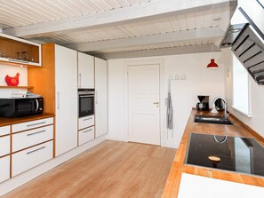 A modern kitchen with white cabinetry, a built-in oven, a microwave, a coffee maker, and a wooden countertop.