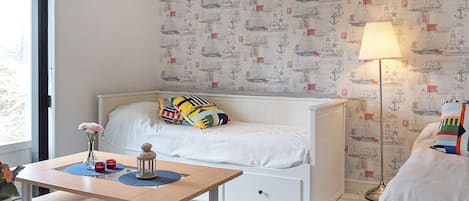 A bedroom with a bed, a bedside table, a lamp, and a wall with nautical-themed wallpaper.