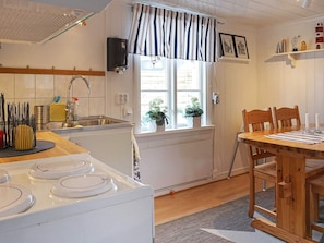 A compact kitchen with a stove, sink, and window with curtains. - 4 Person Holiday Home in Lysekil (Lysekil)
