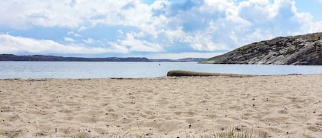 Una playa arenosa con cielo despejado y colinas lejanas.