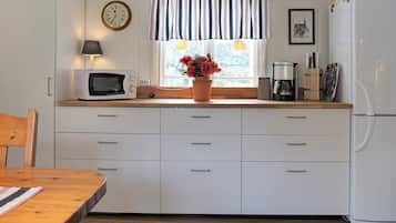 Una cocina con armarios blancos, microondas, cafetera y refrigerador.