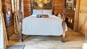 A wooden cabin bedroom with a bed, a painting on the wall, and a wooden floor.