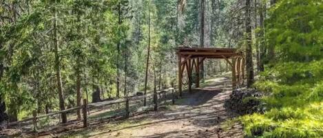 Une zone boisée avec une structure en bois, peut-être un belvédère, située sur un chemin de terre.
