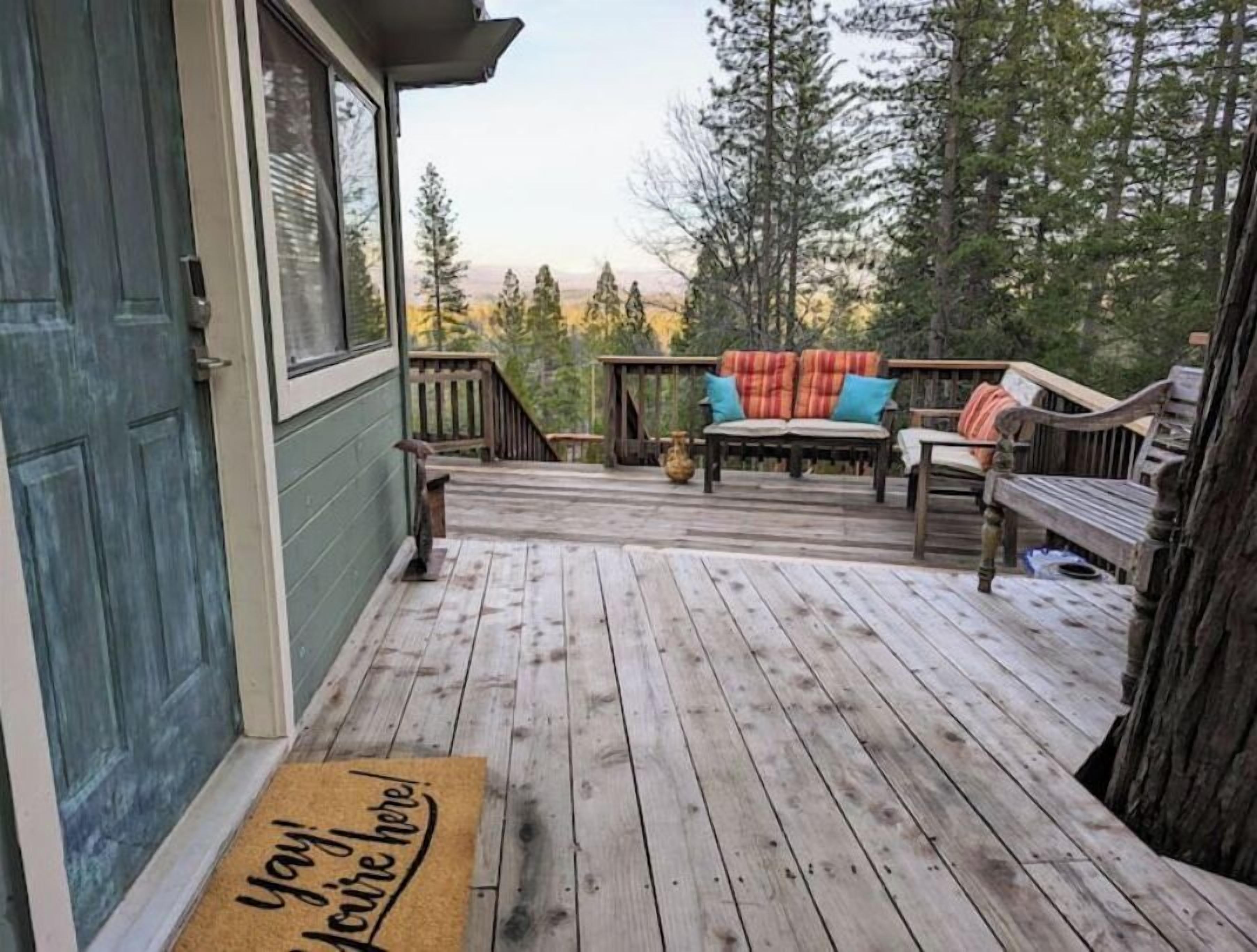 Une terrasse en bois avec des meubles d’extérieur, un paillasson et une vue sur les arbres.
