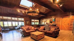 A spacious living room with a large brown leather sofa, a wooden coffee table, and a chandelier.