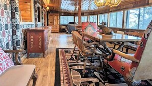 A cozy cabin interior with a wooden ceiling, a dining table, chairs, and a patterned rug.