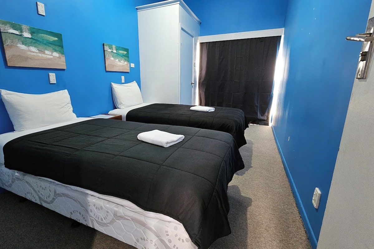 Une chambre avec deux lits, des murs bleus et des œuvres d’art.