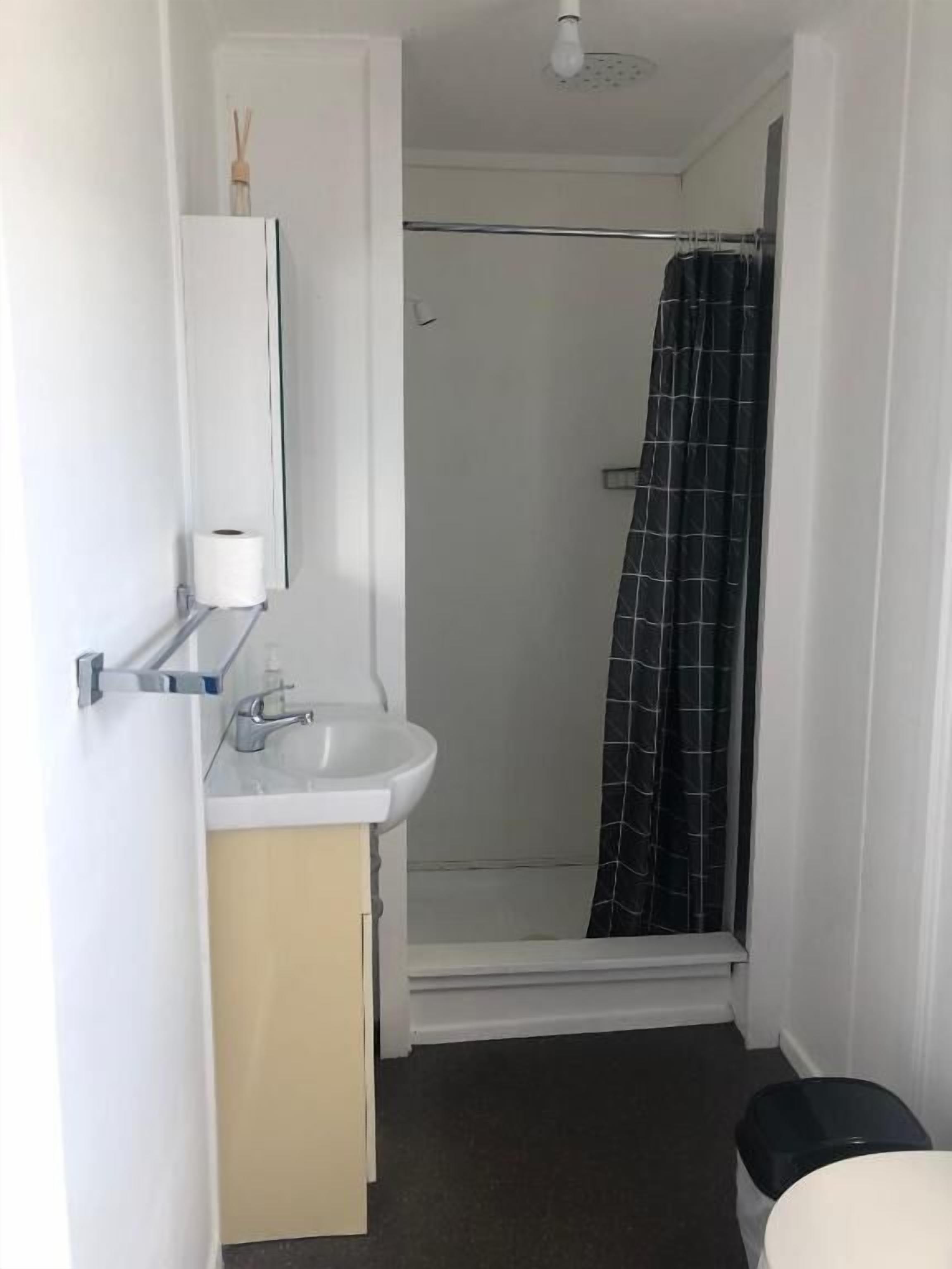 A small, compact bathroom with a white sink, a mirror, a towel rack, and a shower with a black checkered curtain.