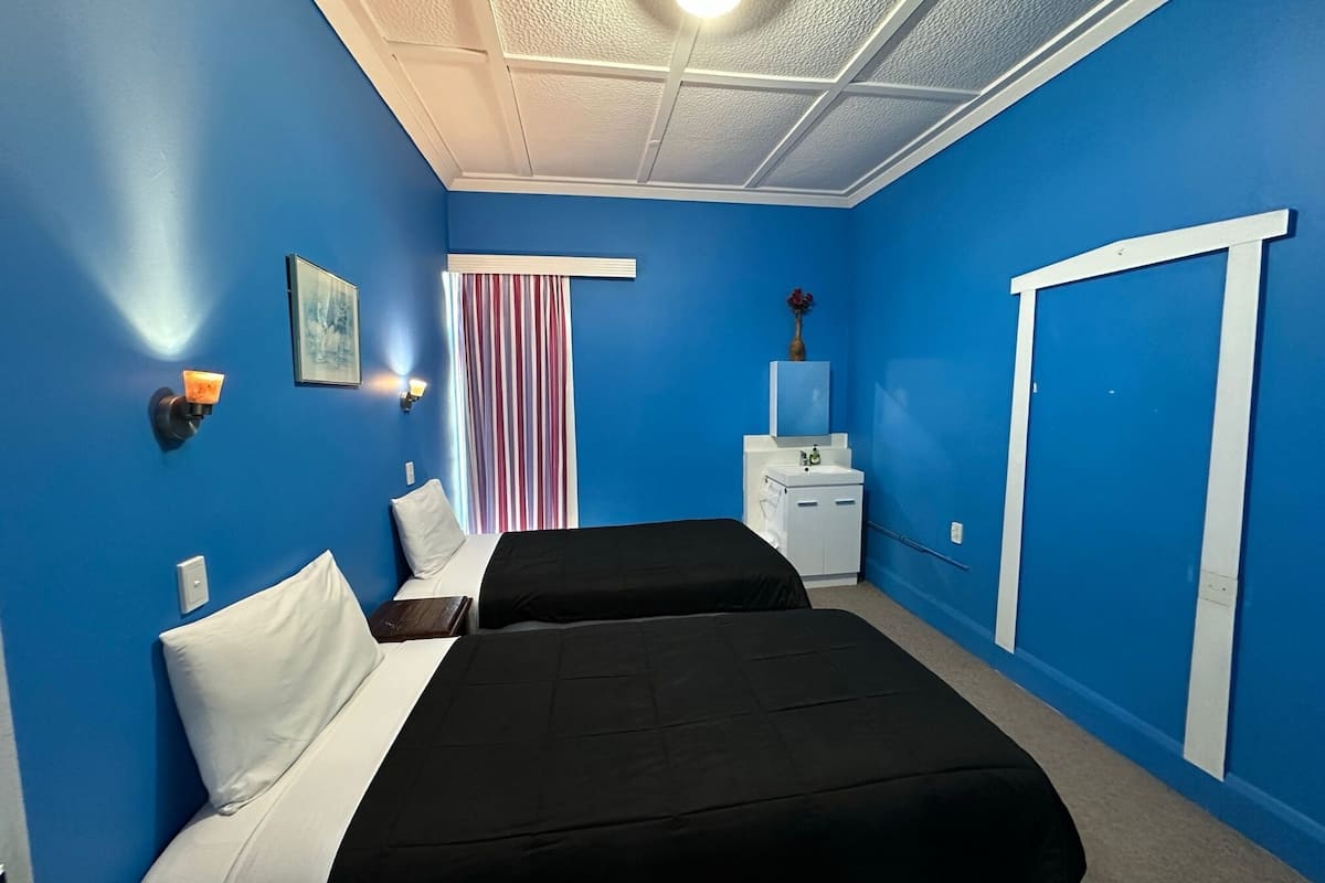 Une chambre avec deux lits, une petite commode blanche, un miroir et une fenêtre avec des rideaux à rayures.