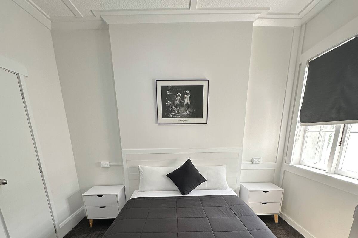 Une chambre à coucher avec un grand lit, une table de chevet, une commode, une fenêtre donnant sur un beau paysage et un tableau encadré accroché au mur.