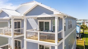A two-story house with a balcony on the upper floor, a covered porch on the ground floor, and a clear blue sky in the background. - Pearl Paradise: with elevator & golf cart included! 2 blocks to beach.  (Carolina Beach)