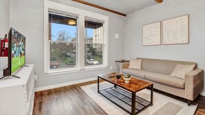 A living room with a beige sofa, a coffee table, and a TV on a stand. - DT Action! | Extended stay | Work, Play, & Relax! (Tacoma)