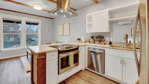 A modern kitchen with a central island, stainless steel appliances, and wooden beams on the ceiling. - DT Action! | Extended stay | Work, Play, & Relax! (Tacoma)