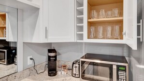 A kitchenette with white cabinets, a coffee maker, a toaster, and a microwave. - DT Action! | Extended stay | Work, Play, & Relax! (Tacoma)