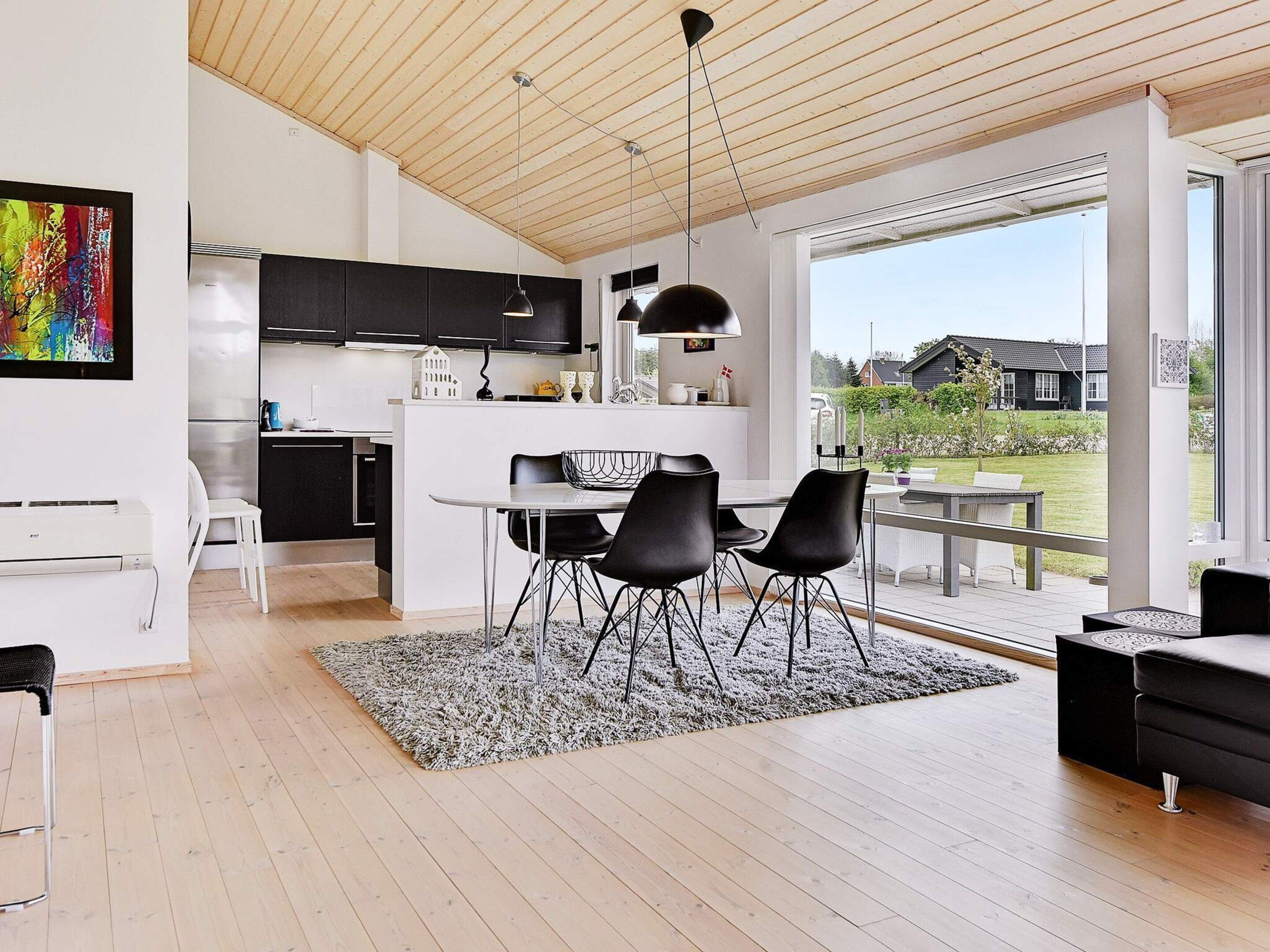 A modern kitchen with black cabinets, a dining area with a table and chairs, and a large window offering a view of the outdoors.