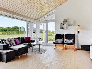 A modern living room with a black sofa, two armchairs, a coffee table, and a floor lamp. Large windows offer a view of the outdoors. - 5 Star Holiday Home in Nordborg (Nordborg)