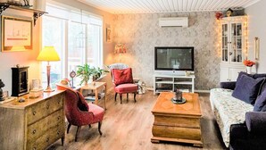 A cozy living room with a wooden floor, a television, a sofa, a red armchair, a coffee table, and a cabinet with decorative lights. - 5 Person Holiday Home in Flen (Flen)