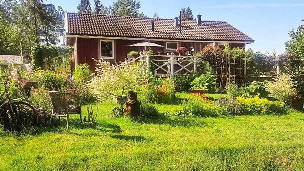 A red house with a tiled roof, surrounded by a well-maintained garden with various plants and flowers. - 5 Person Holiday Home in Flen (Flen)