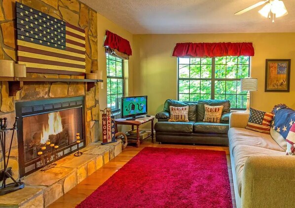 Ein Wohnzimmer mit Kamin aus Stein, einem Fernseher, einem Ledersofa und einem roten Teppich.