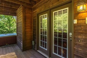 Una cabaña de madera con porche, jacuzzi y vistas al bosque.