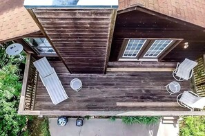Eine Holzterrasse mit Metallveranda, zwei Fenstern und einer kleinen Sitzgelegenheit mit zwei Stühlen und einem Tisch.