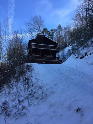Eine Hütte mit Balkon, umgeben von schneebedeckten Bäumen und blauem Himmel.