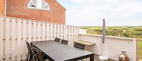 A patio with a table and chairs, a barbecue grill, and a white fence.
