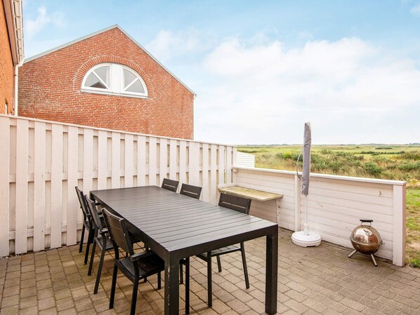 A patio with a table and chairs, a barbecue grill, and a white fence.
