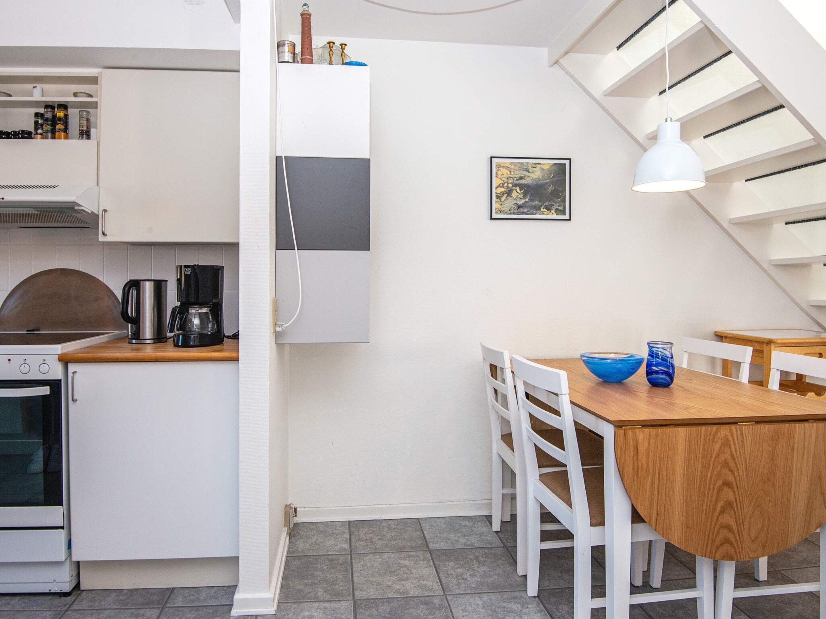 A compact kitchen with a stove, coffee maker, and cabinets. There is a dining area with a table and chairs, and a hanging light fixture.